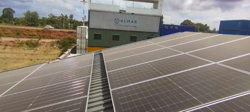 Solar panels on the roof of the Almar Kenya fabrication facility with branded shipping containers in the background.