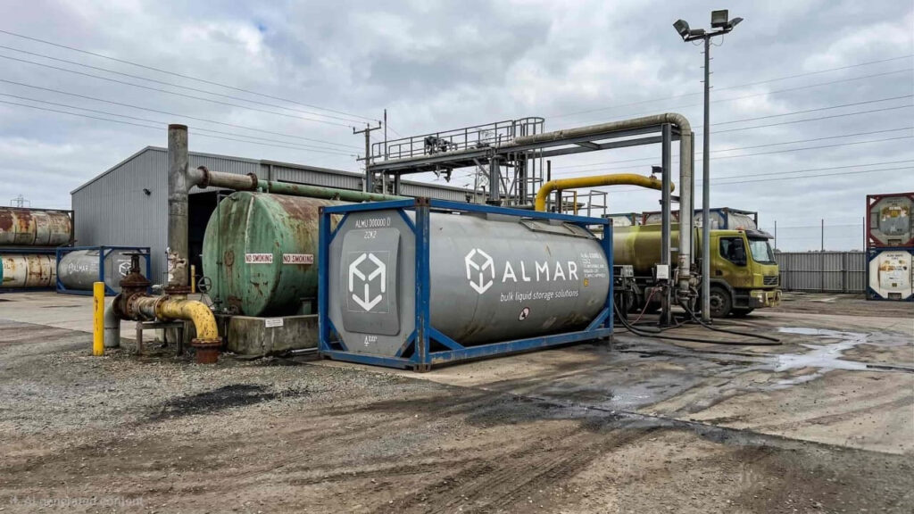 Almar branded ISO Tank container in a logistics yard with industrial piping, tank trailers, and a warehouse.