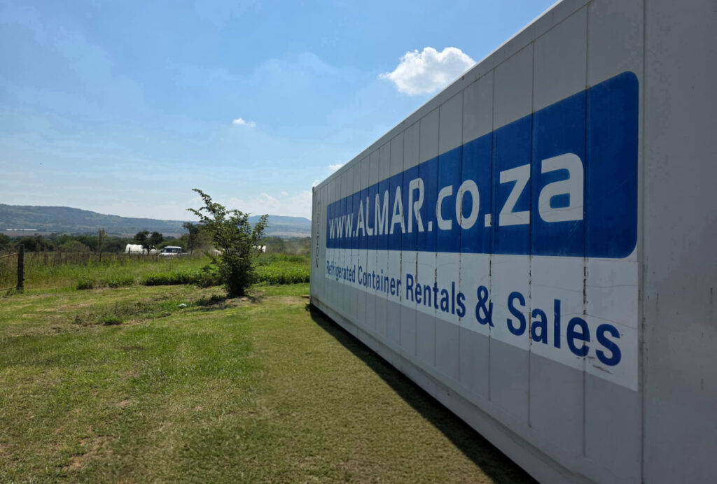 Branded Almar 12m refrigerated container placed on a farm with a landscape of crop fields and distant hills.